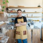 A male potter stands confidently in his ceramic workshop, surrounded by pottery tools and clay creations.